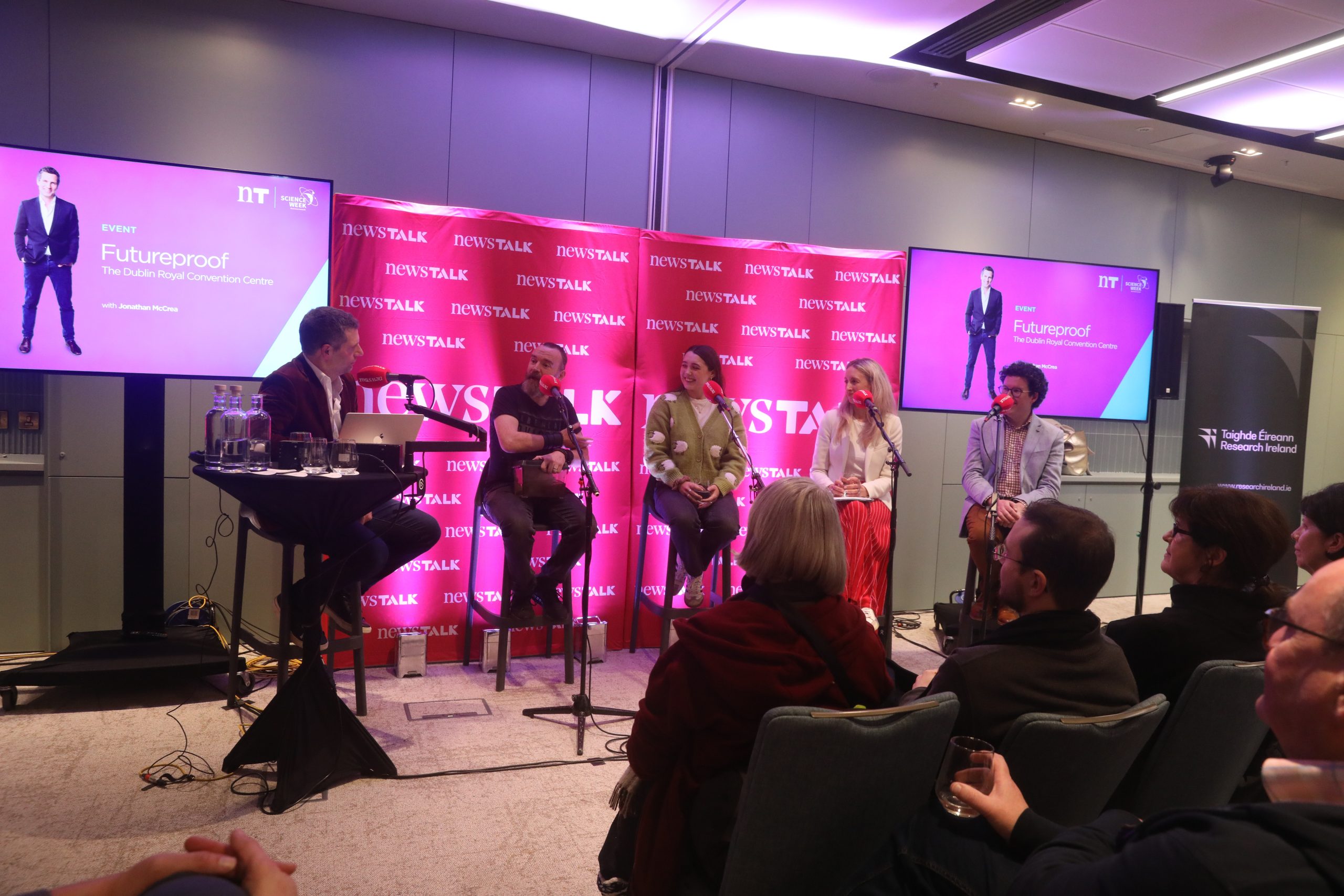 Five-person panel on stage with 'NEWSTALK' backdrop and 'Futureproof' screens, audience seated in front.
