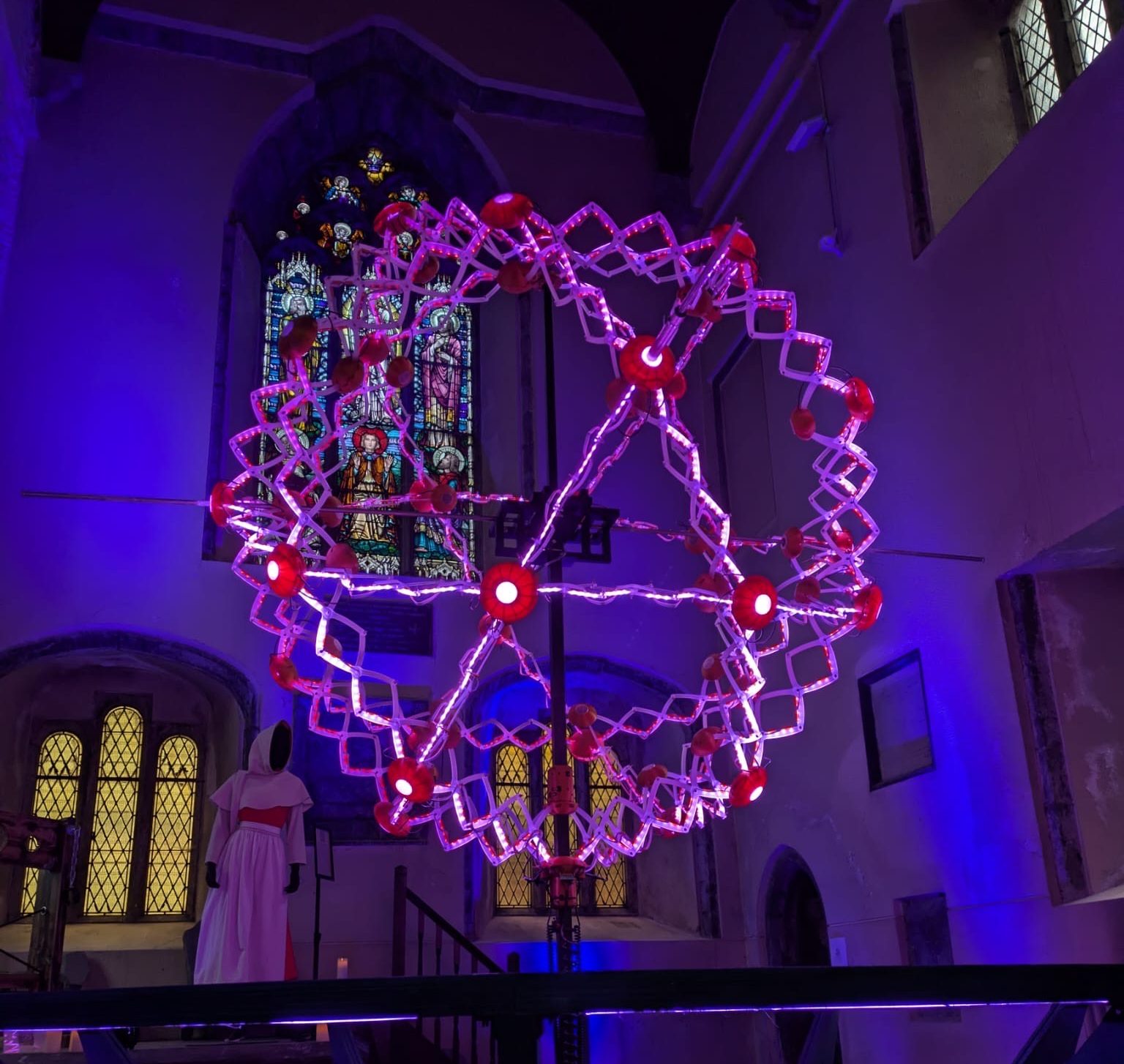 Illuminated geometric structure in pink and red suspended in a church.