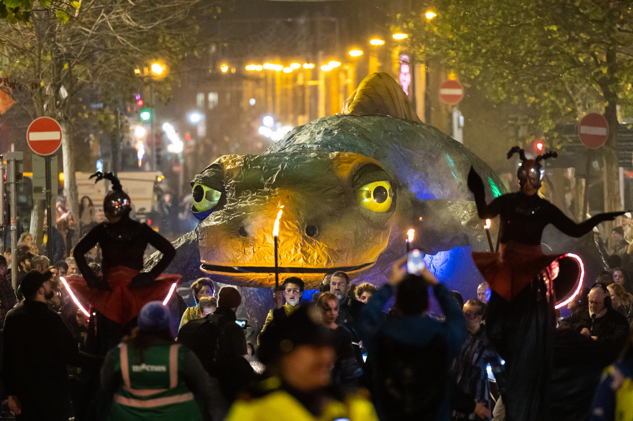Large glowing Newt float in a nighttime street parade with performers and crowd.