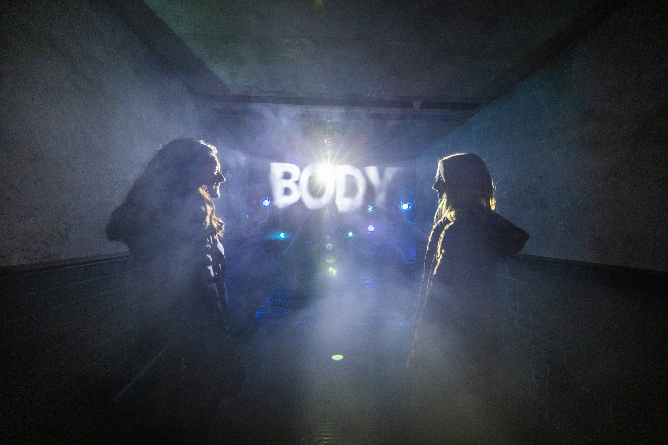 Two people in a foggy corridor facing each other, with 'BODY' illuminated in the background.