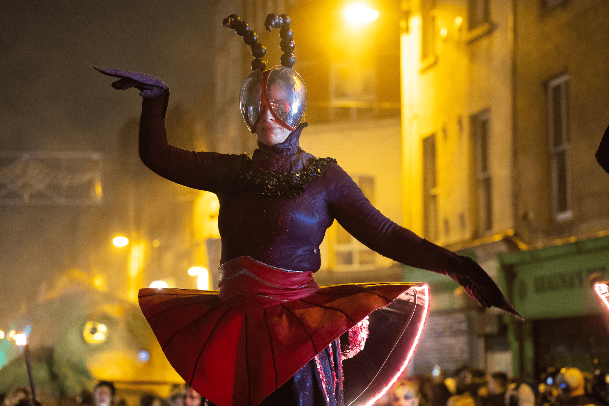 Person walking through a dark outdoor space with glowing red lasers forming a DNA shape and colourful light structures.