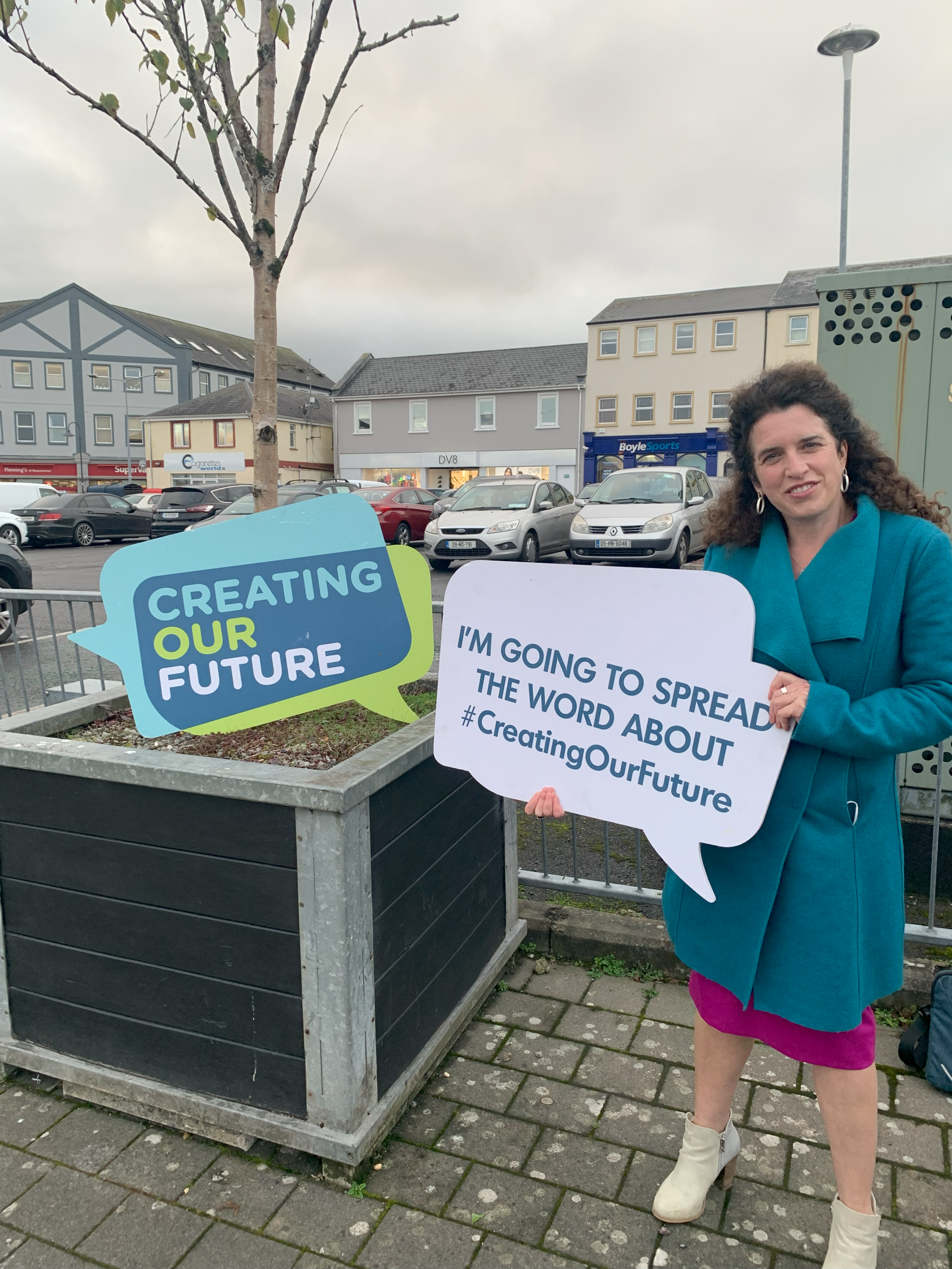 Woman holding Creating Our Future sign outside in town.