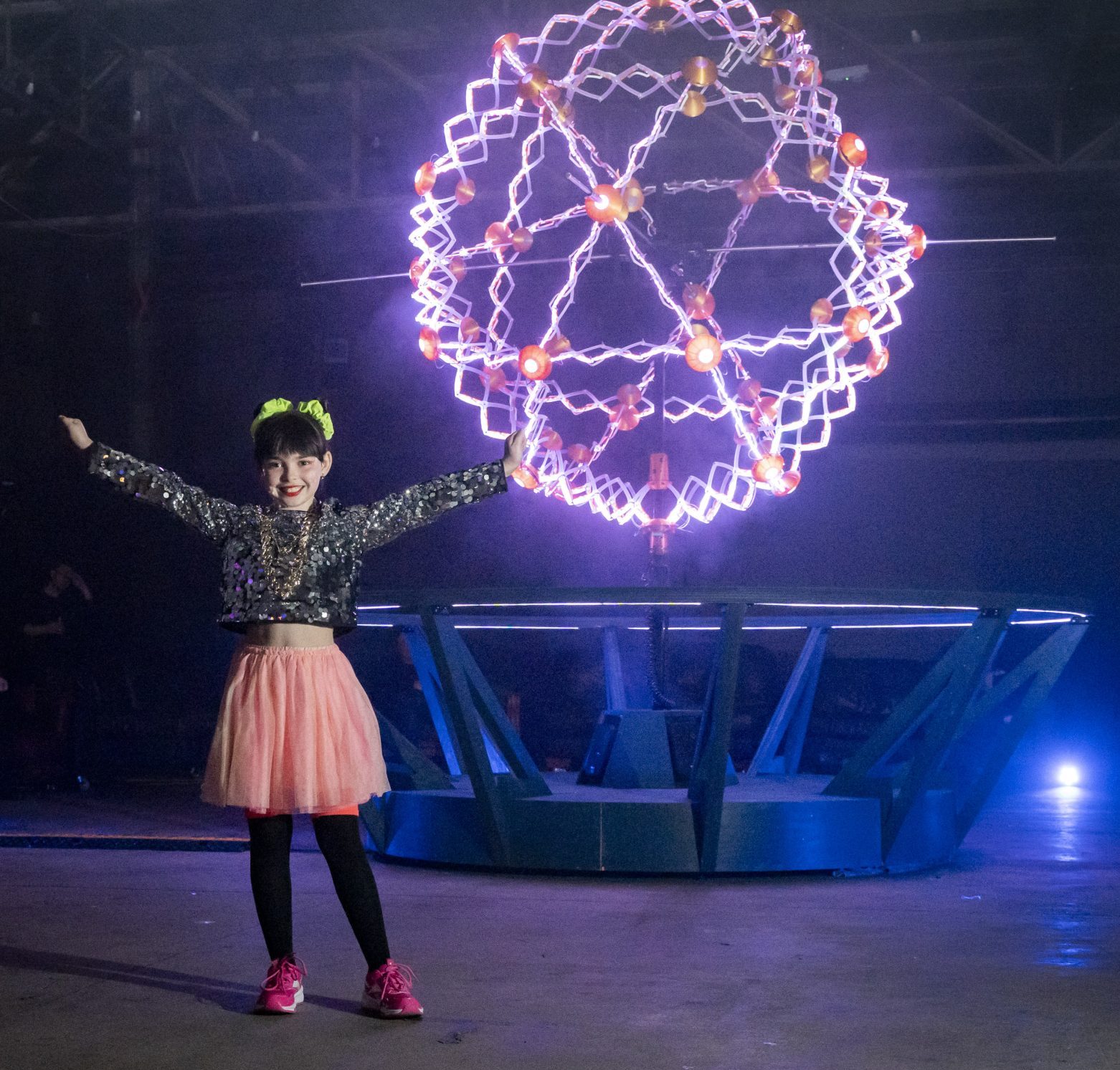 A young girl standing with her arms out in front of a large glowing sphere.