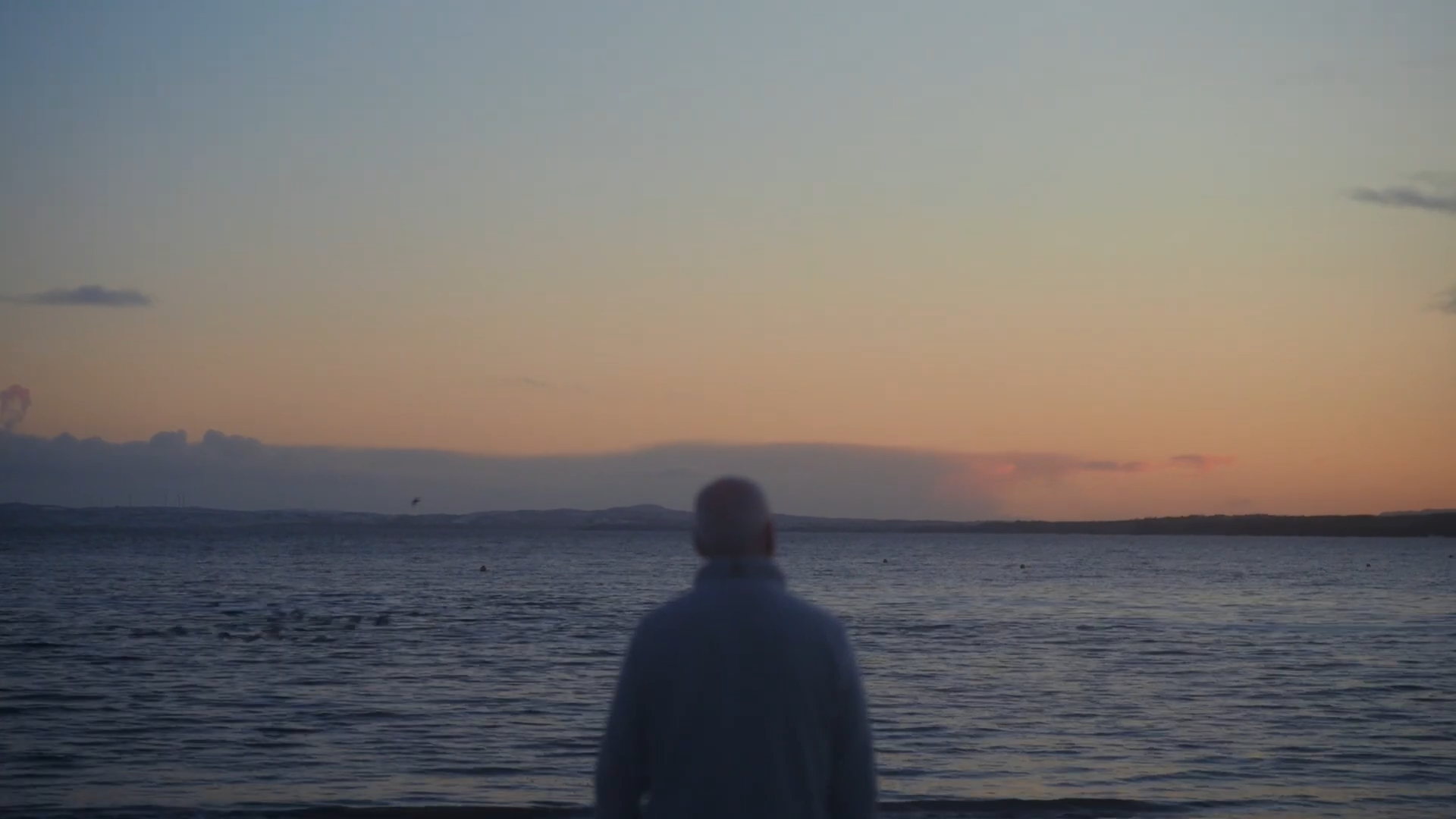 Man looks out on the coast as sun sets.