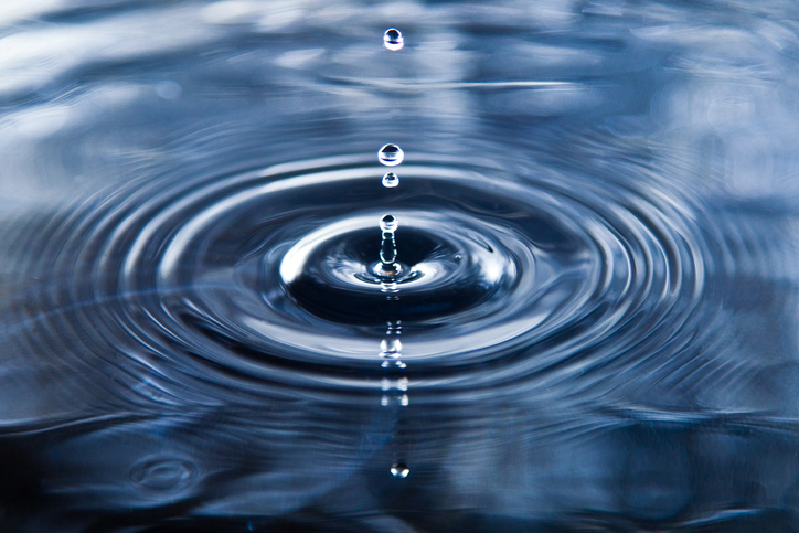 Close-up of water droplets falling into a pool, creating concentric ripples on a blue water surface.