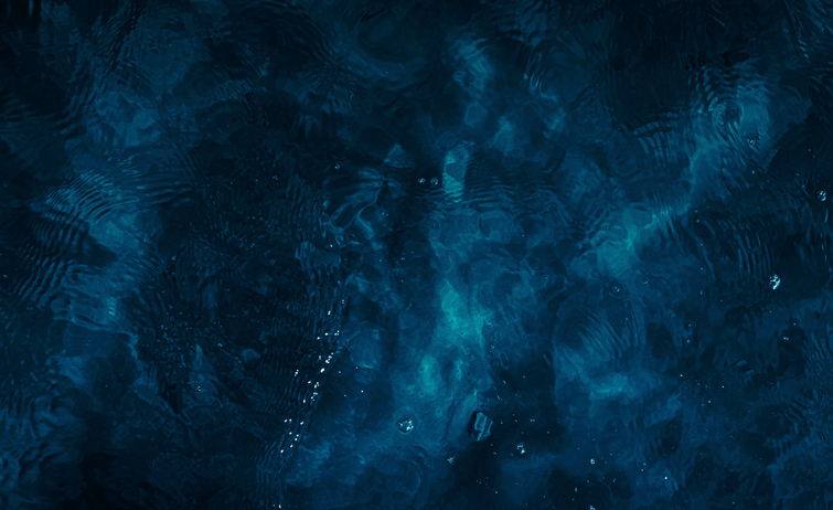 Abstract view of dark blue water with ripples, reflections and subtle movement across the surface.
