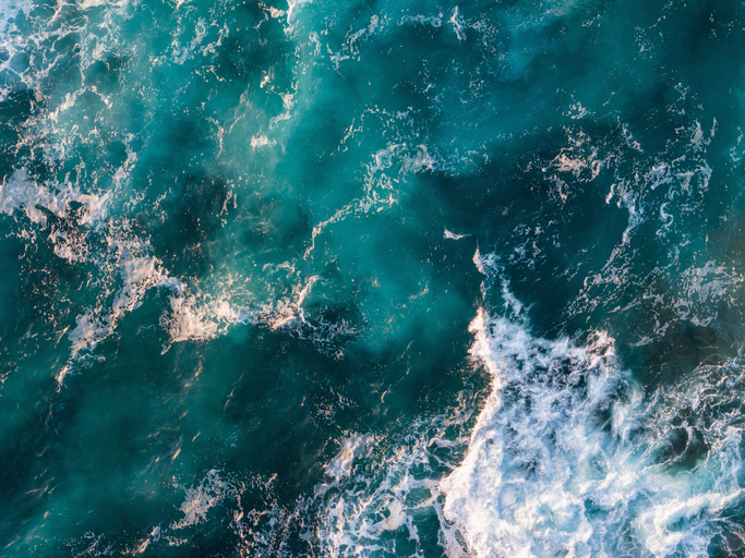 Aerial view of turquoise ocean water with swirling waves and white sea foam.